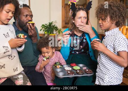 Multiethnic family eating decorated Halloween cupcakes Stock Photo
