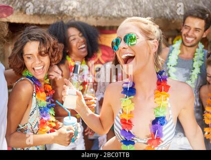 Playful friends wearing leis drinking and partying at sunny summer poolside Stock Photo