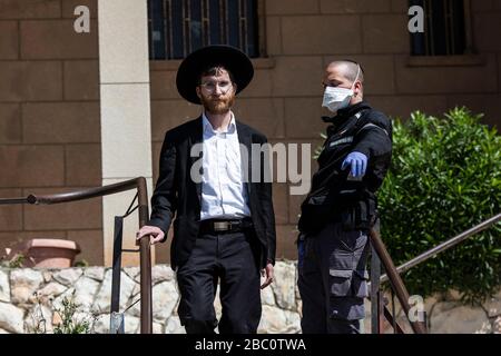 Bnei Brak, Israel. 02nd Apr, 2020. An Israeli policeman leads an Orthodox Jewish man out of the Ponevezh Yeshiva, a Jewish institution that focuses on the study of traditional religious texts, where he and others insist on carrying on with their prayer despite the imposed lockdown amid the coronavirus pandemic. Credit: Ilia Yefimovich/dpa/Alamy Live News Stock Photo