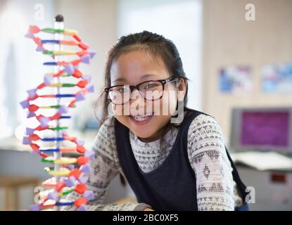 Portrait smiling, confident girl student next to DNA model in classroom Stock Photo