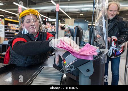 CLEANING OF THE CASH REGISTER AND CREDIT CARD TERMINAL AFTER EACH CUSTOMER, CASHIER AT A SUPERMARKET WEARING A PROTECTIVE FACE MASK AND GLOVES, PREVENTIVE HEALTH MEASURE PUT IN PLACE FOR THE CORONAVIRUS EPIDEMIC, RUGLES, NORMANDY, FRANCE