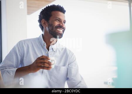 Smiling, enthusiastic man drinking coffee and looking away Stock Photo