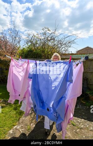 Woman hanging out various coloured mens shirts on a rotating washing line during in the wind in back garden UK Stock Photo