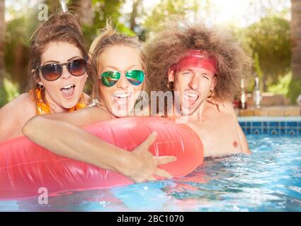 Portrait exuberant, playful young friends with inflatable raft in summer swimming pool Stock Photo