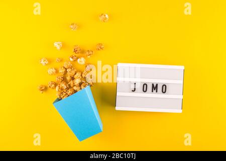 Abbreviation word JOMO written on a decorative board on a bright yellow background. The concept of relaxation from information and gadgets. Top view, flat lay. Stock Photo