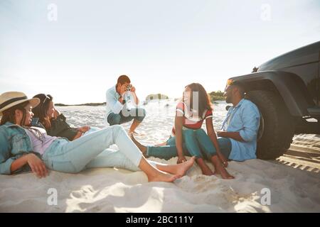 Young man with digital camera photographing friends hanging out on sunny beach Stock Photo