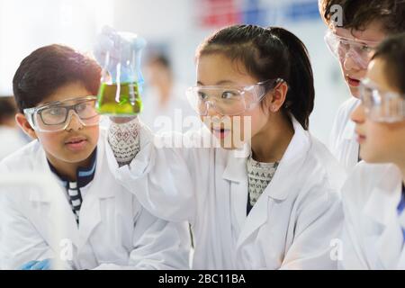 Curious students examining liquid in beaker, conducting scientific experiment in laboratory classroom Stock Photo