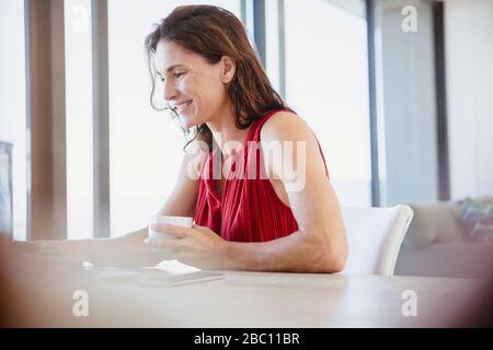 Smiling brunette woman drinking coffee and working at dining table Stock Photo