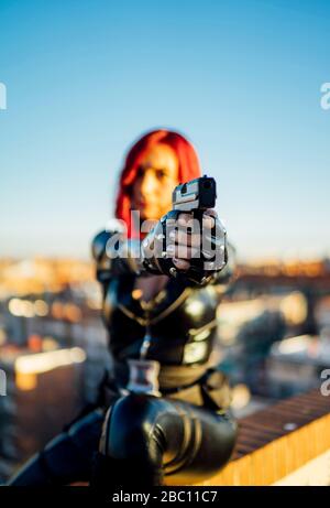 redheaded woman wearing black leather catsuit on rooftop aiming with gun 2bc11c7