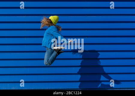 Teenage girl jumping in the air in front of blue background Stock Photo