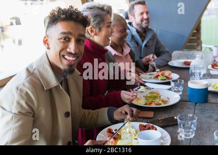 Portrait smiling young man eating breakfast with friends at restaurant outdoor patio Stock Photo