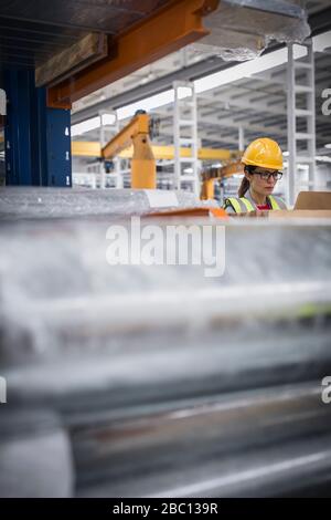 Focused female worker using laptop in steel factory Stock Photo