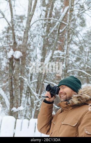 Portrait of smiling man taking photo with digital camera in winter forest Stock Photo