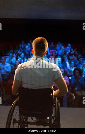 Female speaker in wheelchair on stage talking to audience Stock Photo