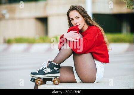 Portrait of young woman with roller skates sitting on a wall in the city Stock Photo