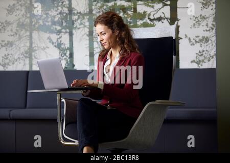 Businesswoman sitting in armchair in office using laptop Stock Photo