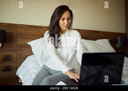 Businesswoman sitting on bed in hotel room using laptop Stock Photo