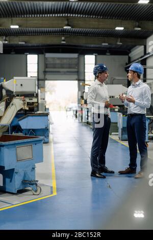 Two men wearing hard hats talking in a factory Stock Photo