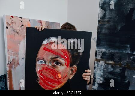 Female painter hiding behind painting in her studio Stock Photo