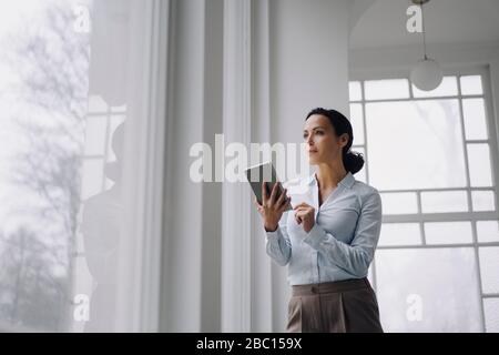 Successful businesswoman, standing by window, using digital tablet Stock Photo