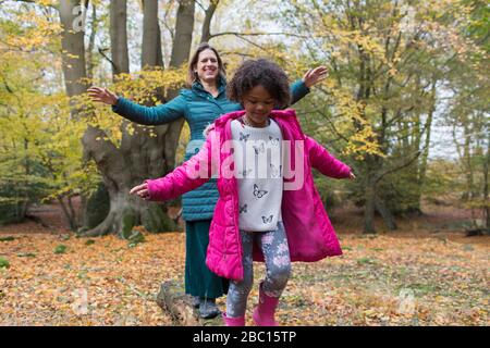 Mother and daughter balancing on fallen log in autumn woods Stock Photo