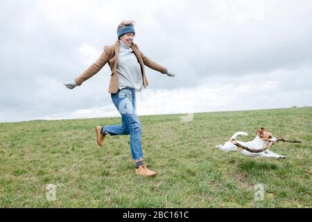 Smiling mature woman playing with her dog on a meadow Stock Photo