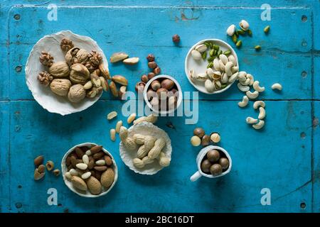 Overhead view of various nuts in bowls on blue rustic table Stock Photo