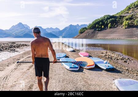 Man carrying paddle, sup boards at lakeside Stock Photo