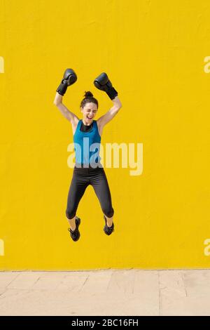 Young female boxer jumping in front of a yellow wall Stock Photo