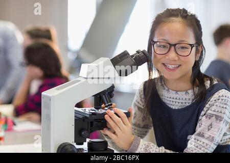 Portrait smiling, confident girl student using microscope, conducting scientific experiment in laboratory classroom Stock Photo