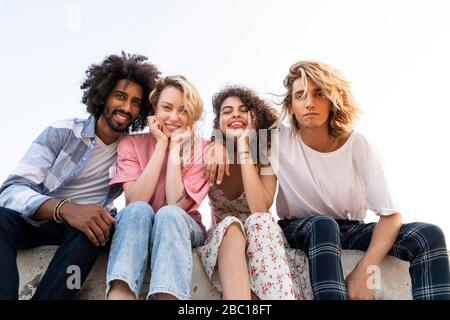 Portrait of happy friends sitting on a wall outdoors Stock Photo