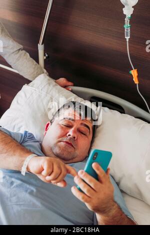 Patient lying in hospital bed using cell phone Stock Photo