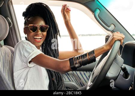 Portrait of laughing woman with dreadlocks driving car Stock Photo