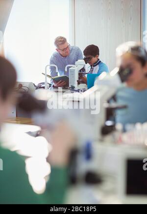 Male teacher and boy student using microscope, conducting scientific experiment in laboratory classroom Stock Photo
