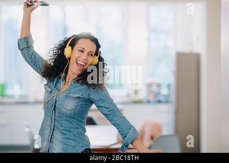 Happy woman listening music, singing and dancing, using smartphone and headphones Stock Photo