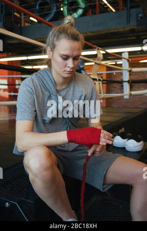 Young woman tying bandage around her hand in boxing club Stock Photo
