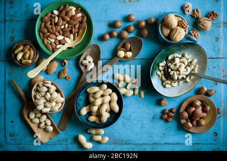 Overhead view of various nuts in bowls and on spoons on blue rustic table Stock Photo