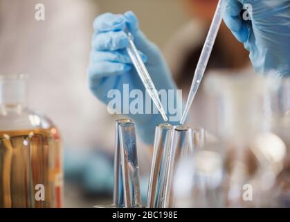 Hands in rubber gloves using pipettes over test tubes, conducting scientific experiment Stock Photo