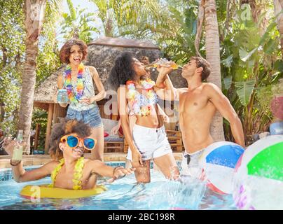 Playful young friends drinking and playing in sunny summer swimming pool Stock Photo