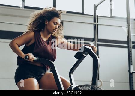 Young woman doing air bike workout in gym Stock Photo
