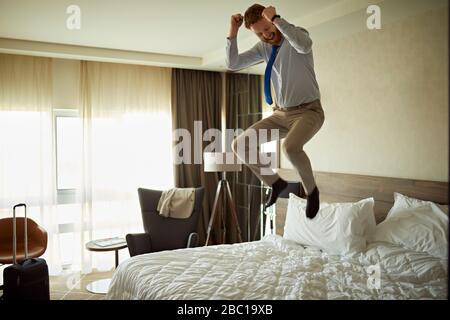 Excited businessman jumping on bed in hotel room Stock Photo