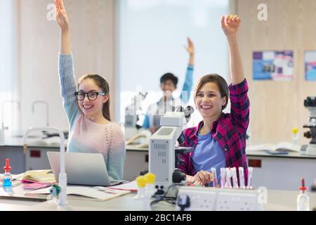 Eager, smiling students raising hands in science laboratory classroom Stock Photo
