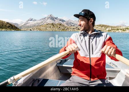 Young smiling man in a rowing boat, Lake Suretta, Graubuenden, Switzerland Stock Photo