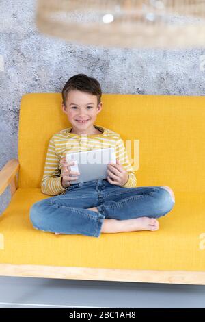 Boy playing with tablet on yellow couch Stock Photo
