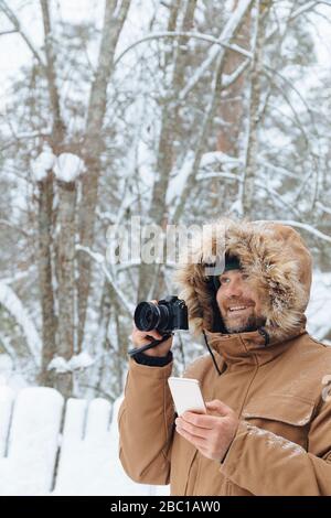 Portrait of relaxed man with digital camera and mobile phone in winter forest Stock Photo