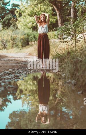Red-haired woman posing in front of a puddle, mirrored Stock Photo
