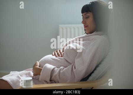 Serene pregnant woman in bathrobe holding stomach Stock Photo