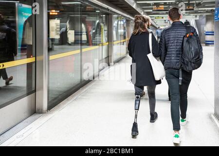 Rear view of young woman with leg prosthesis and man walking at subway station platfom Stock Photo