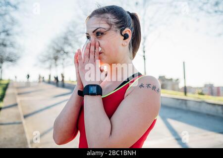 Sporty young woman with wireless earphones blowing her nose Stock Photo
