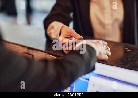 Close-up of woman paying contactless with credit card at reception desk Stock Photo
